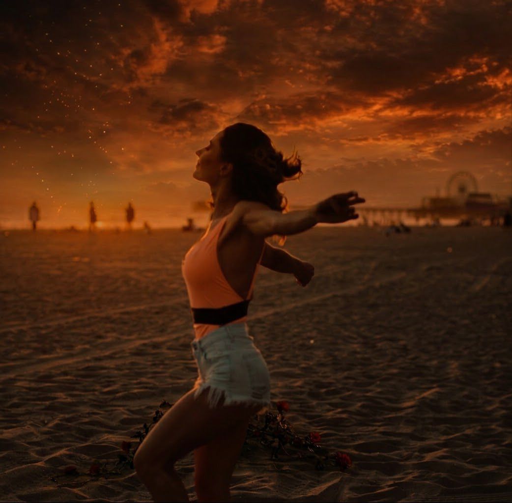 A woman opening her arms on a beach beneath a burning sunset sky