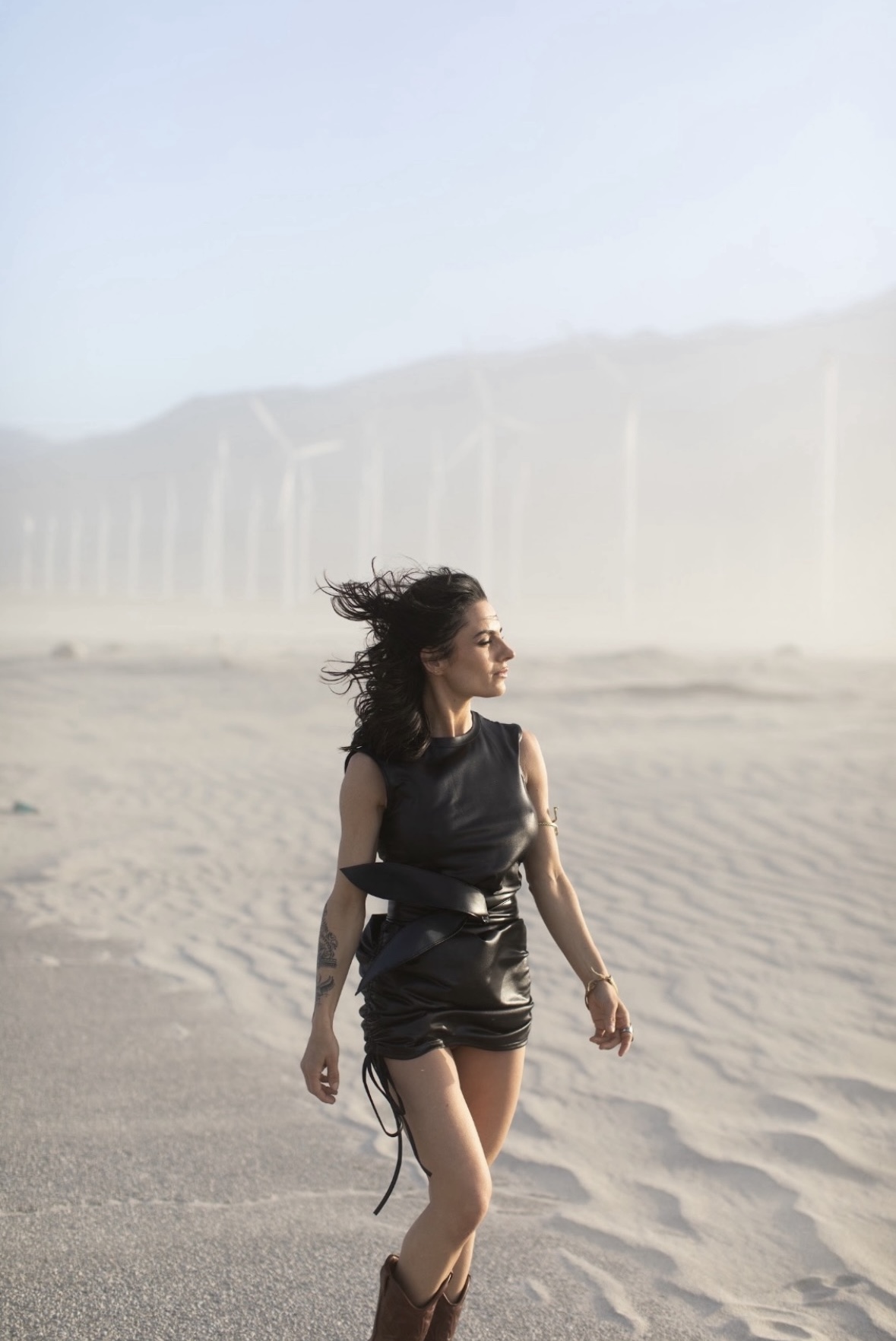 Woman walking through wind-blown desert sand at golden hour